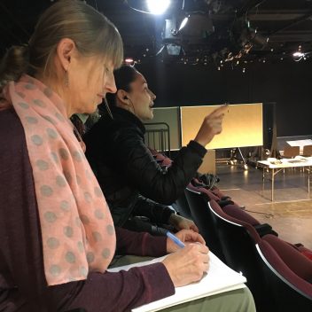 Patti Flather, and Reneltta Arluk sitting on theatre seating, making notes.