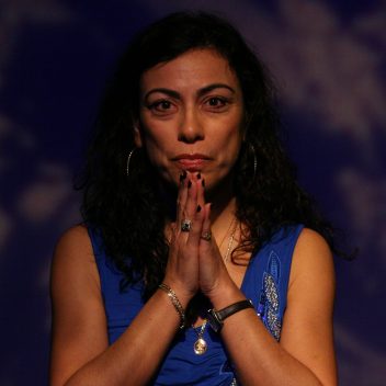 Close up of Carmen Aguirre with their hands in front of their chin, pressed together.