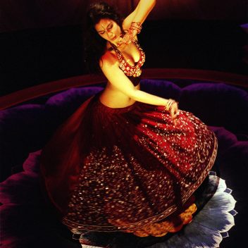 Anita Majumdar spinning with a red outfit on. The background is red and the floor is dark, with some purple and pink