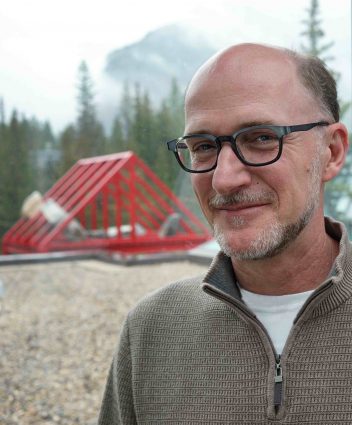 Close up of Brian Quirt, outside with a red structure on the background