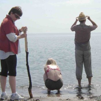 Five people on a beach. One is side profile. The rest have their backs facing us, with one is sitting on their heels.