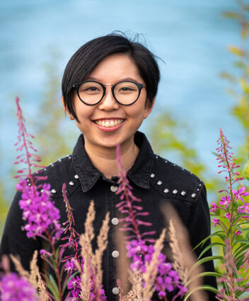 Gloria smiling at the camera, with pink flowers in front of her